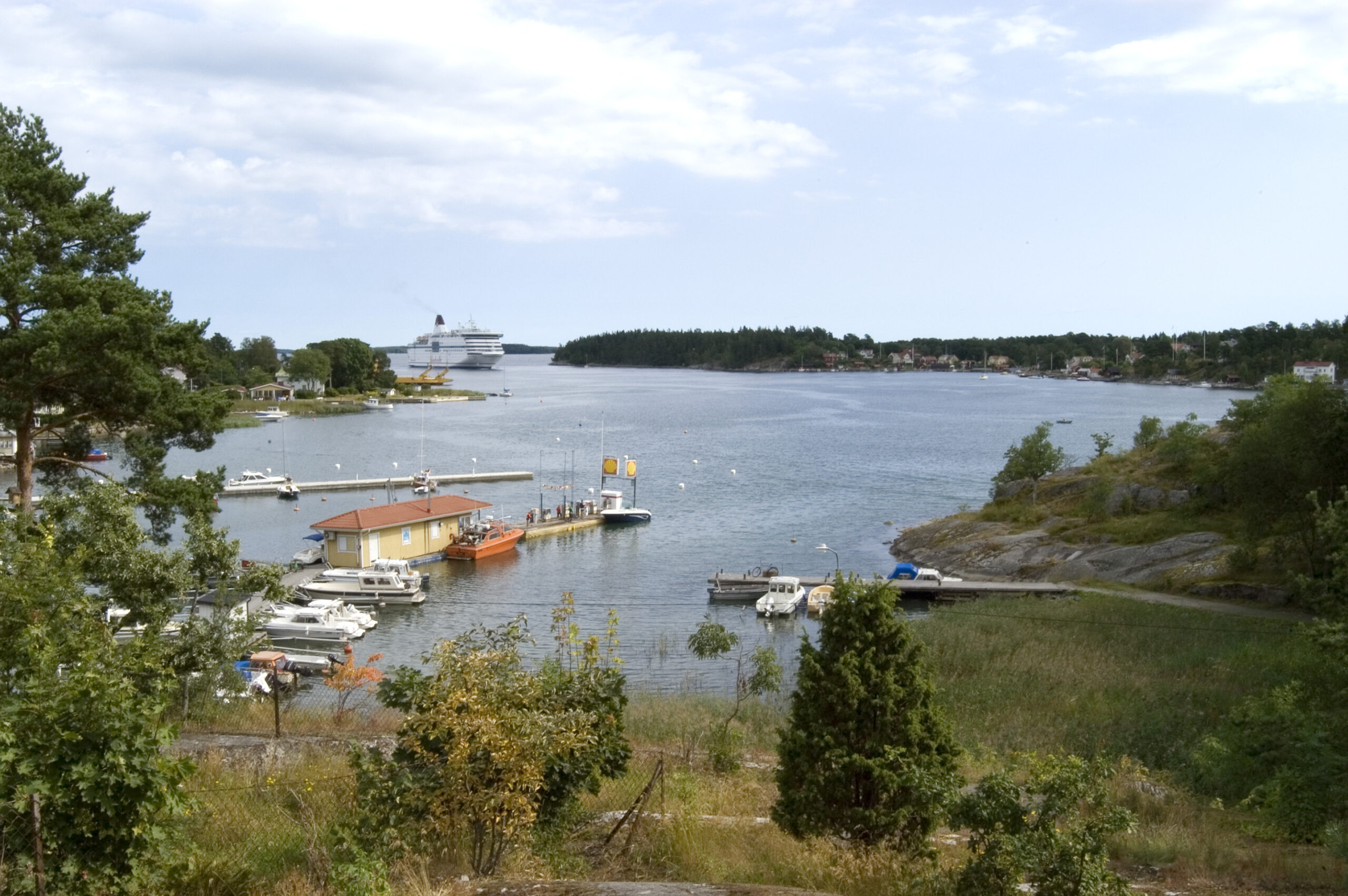 Vy över gräs och vatten. Långt bort kommer en stor båt.