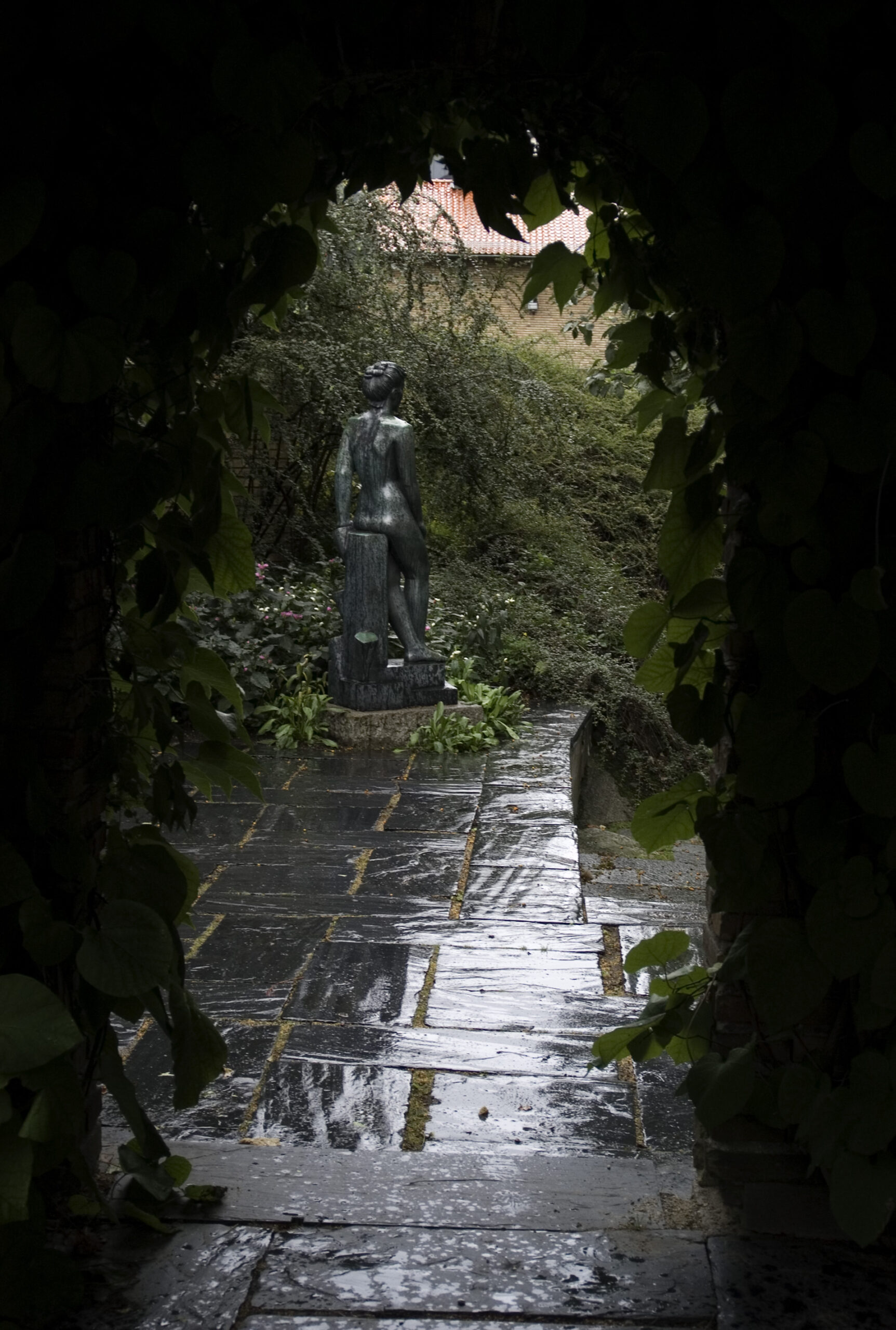 En skulptur av en naken kvinna av sten syns mellan träden.