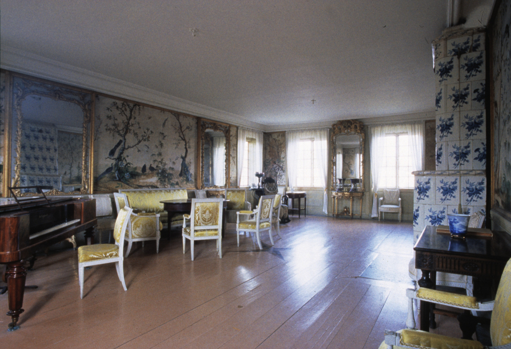 Ett rum med stolar, en kamin och speglar.