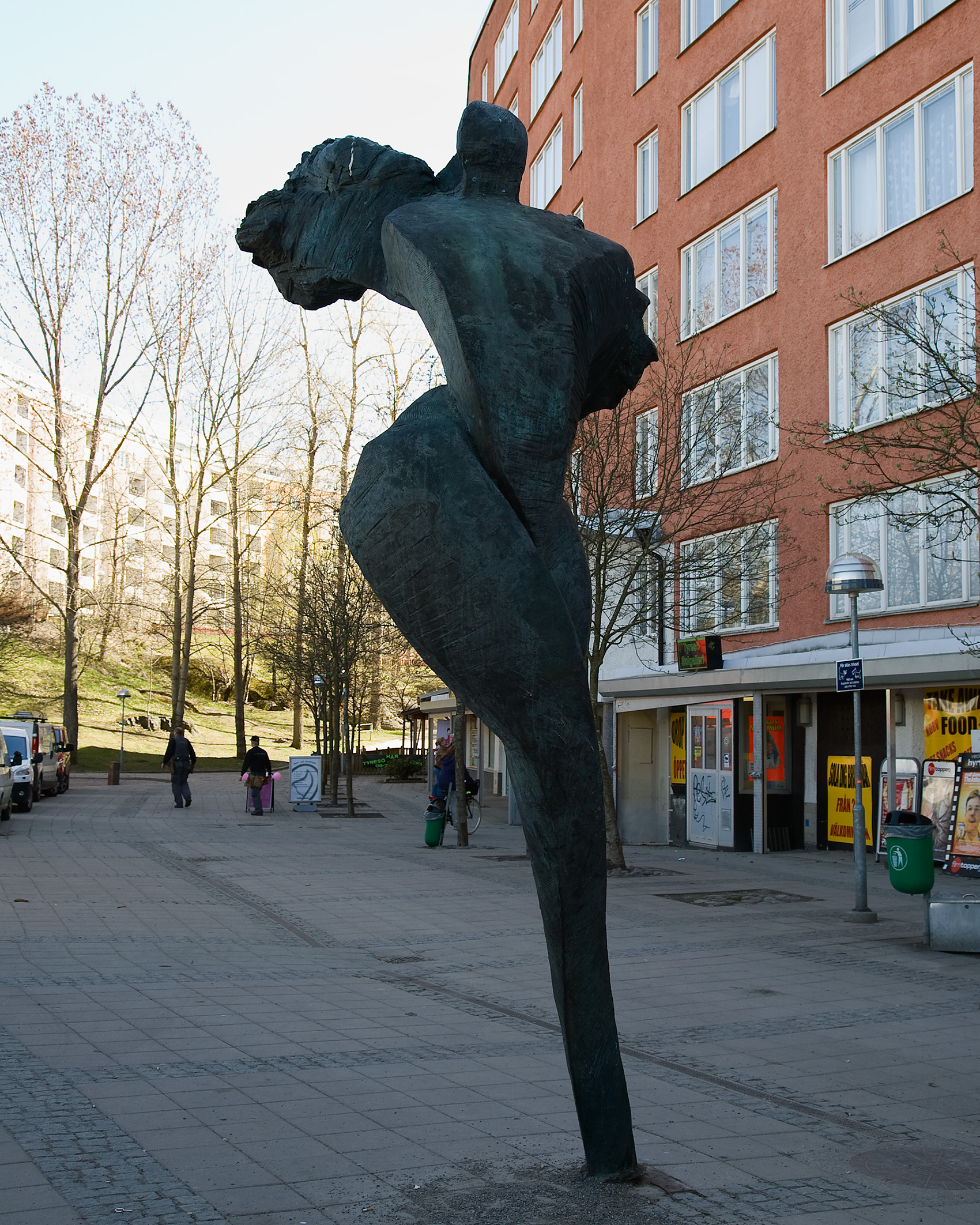En skulptur av en figur med vingarna utsträckta bakåt mot skyn. I gatumiljö.