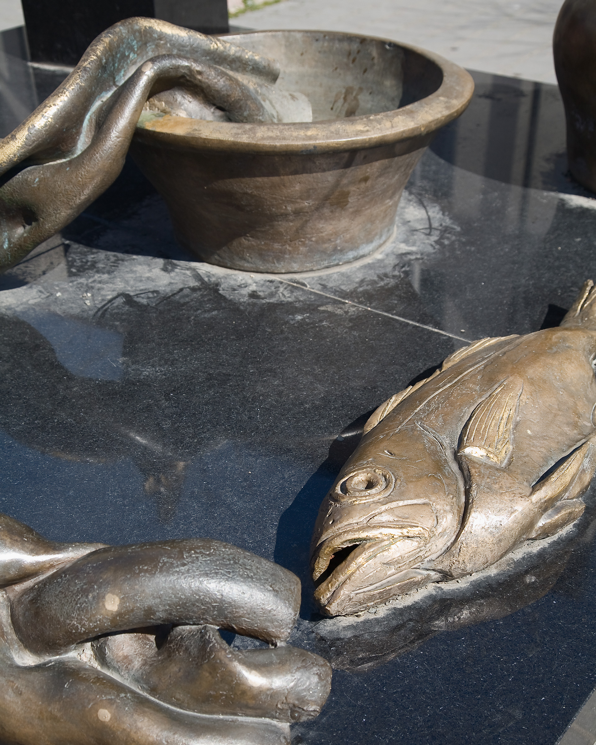 En skulptur av en fisk som ligger på en svart yta med skål av brons bakom.