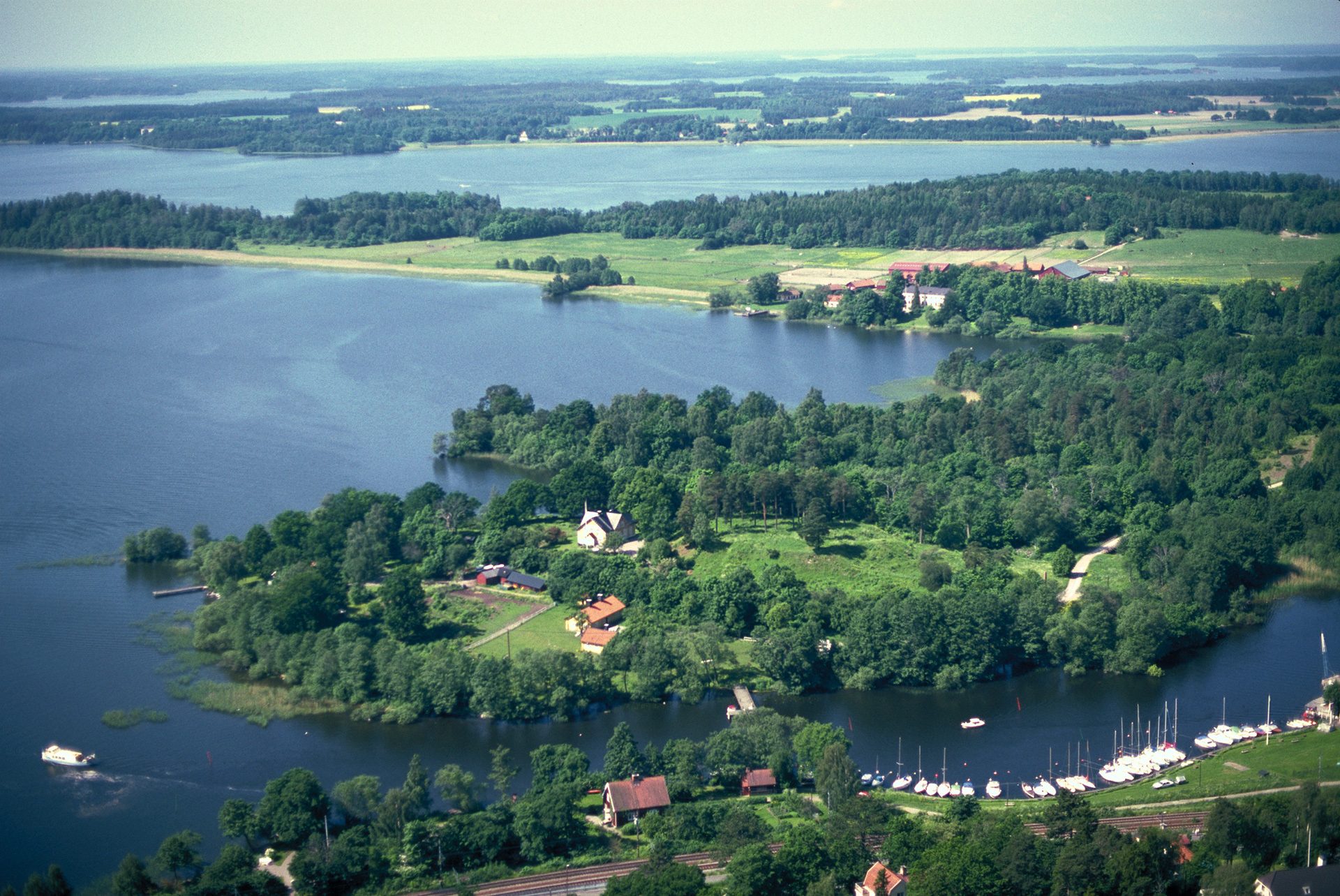 Vy över skog, vatten och några hus.