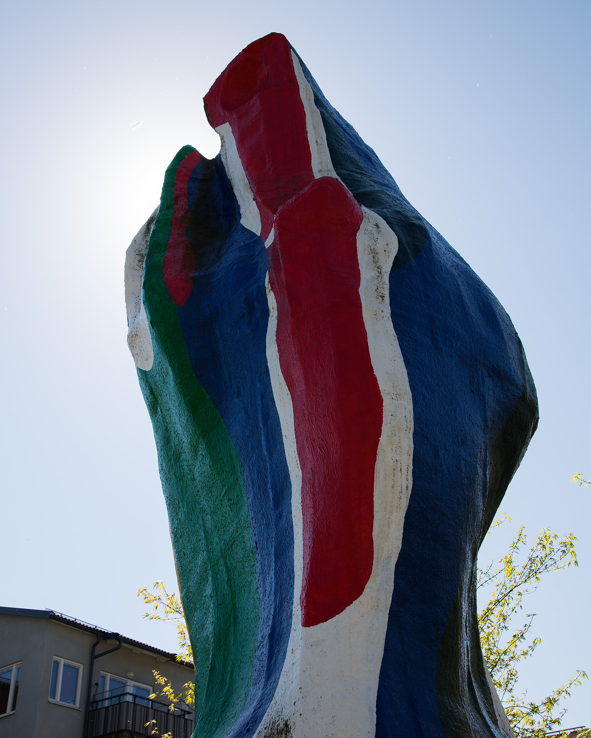 En abstrakt skulptur i färgerna blått, rött, grönt, vitt. Himmel i bakgrunden.