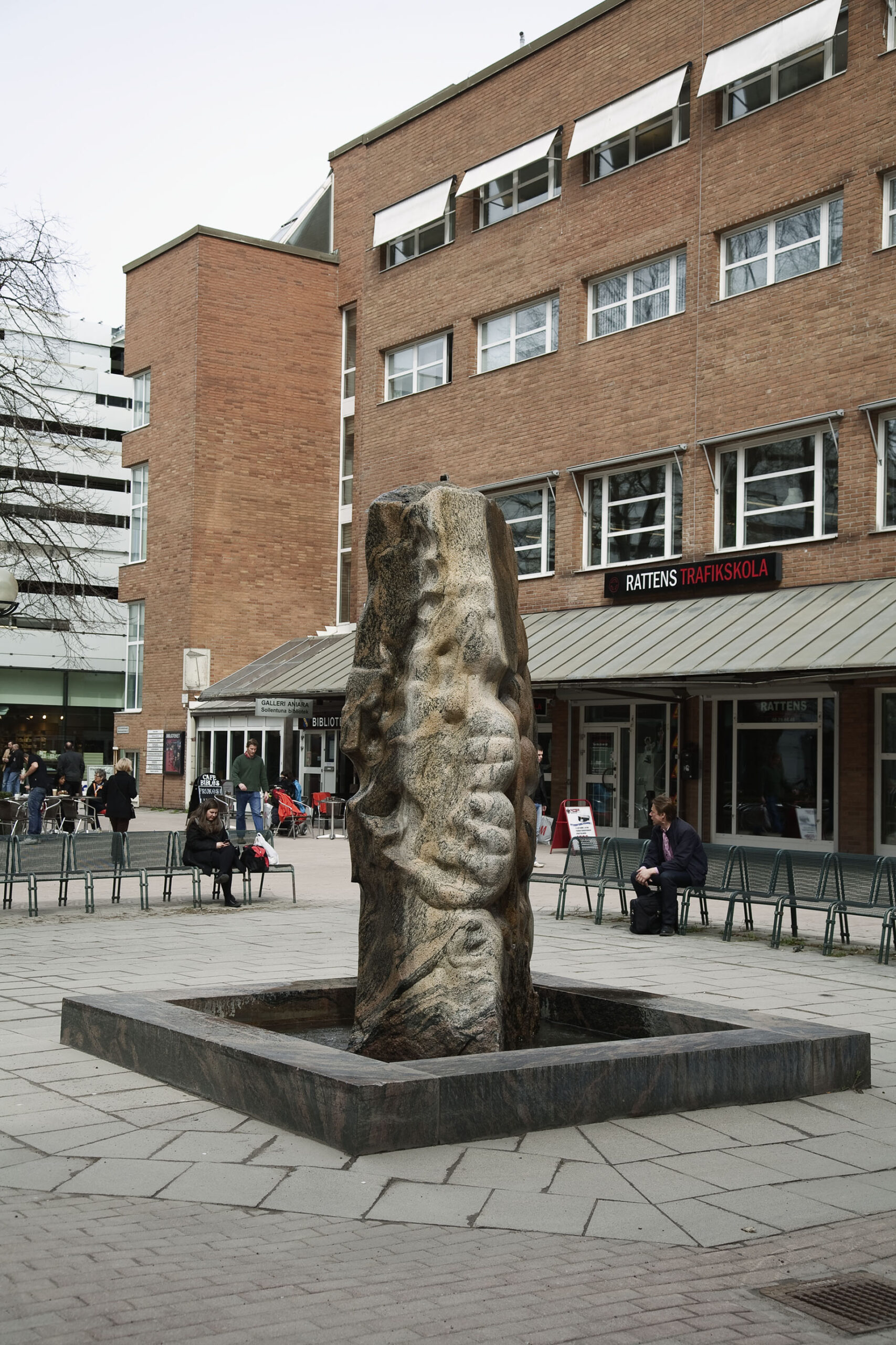 En skulptur i form av en hög abstrakt sten i en fyrkantig form i torgmiljö.