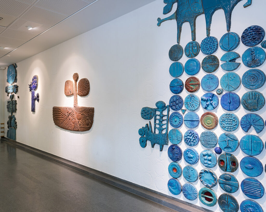 Runda blåa kakelplattor på en vit vägg i en korridor. Abstrakta bruna och blåa former lite längre bort väggen.