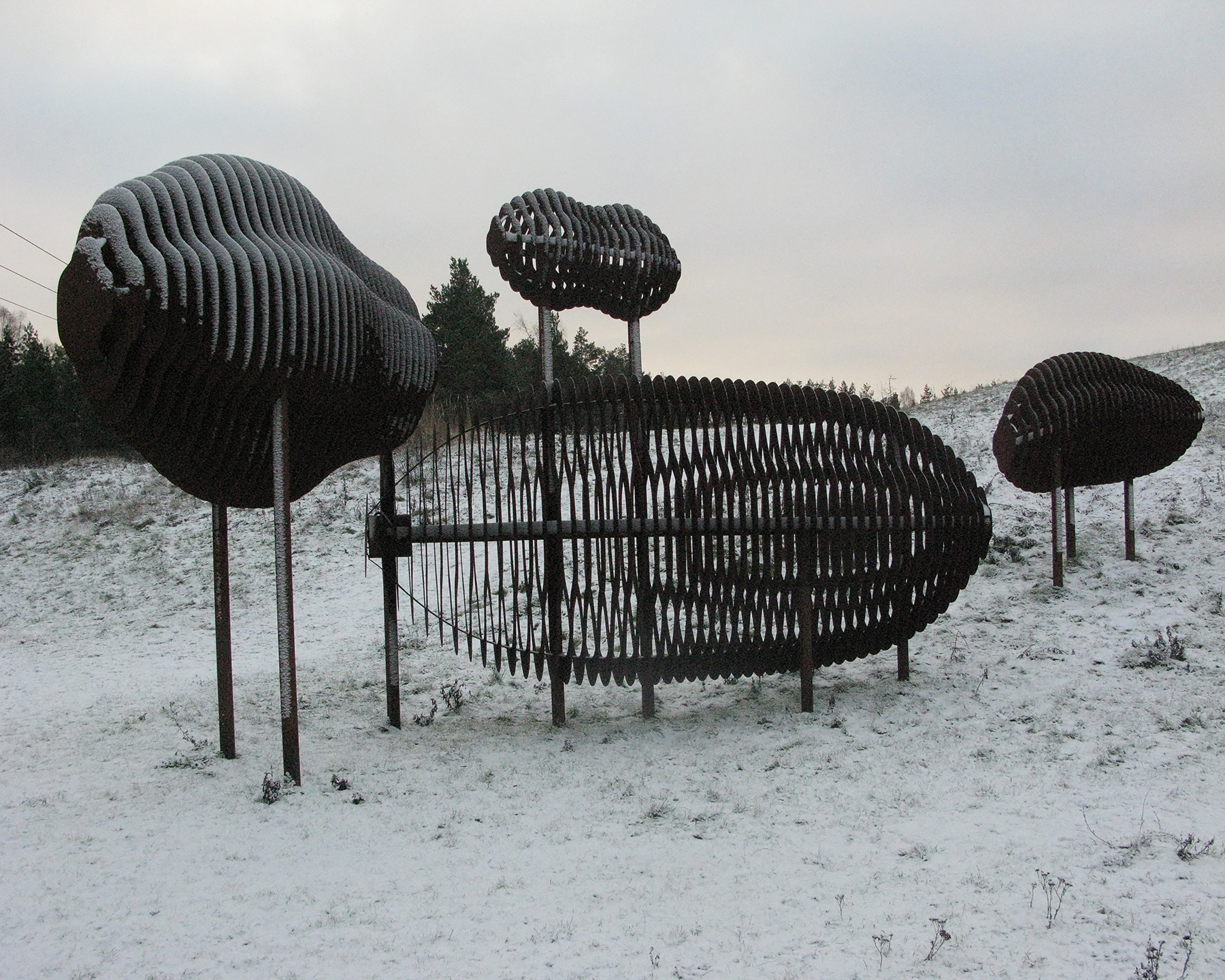 Fyra bruna cylinderformade skulpturer i olika höjder och former står på snöklädd mark.