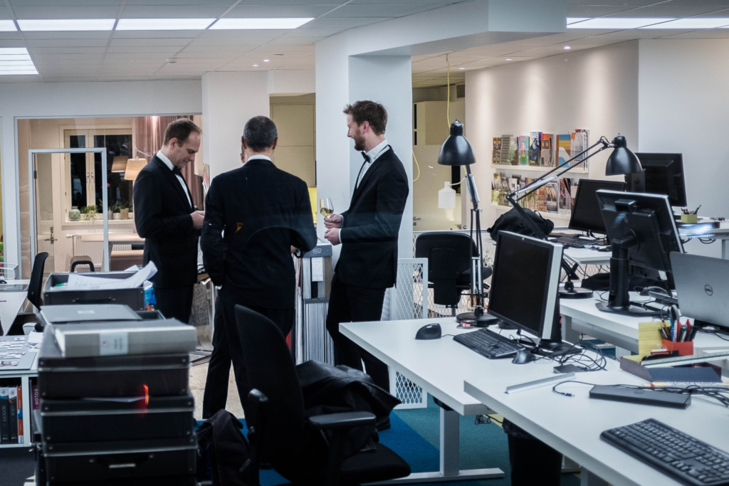 Några män i smoking dricker vin på jobbet.