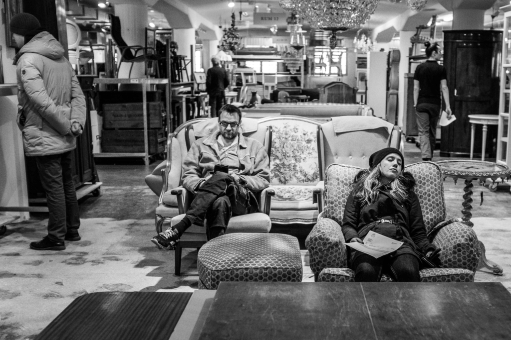 En flicka sover och en man tittar på mobilen på Auktionsverket vid Frihamnen.