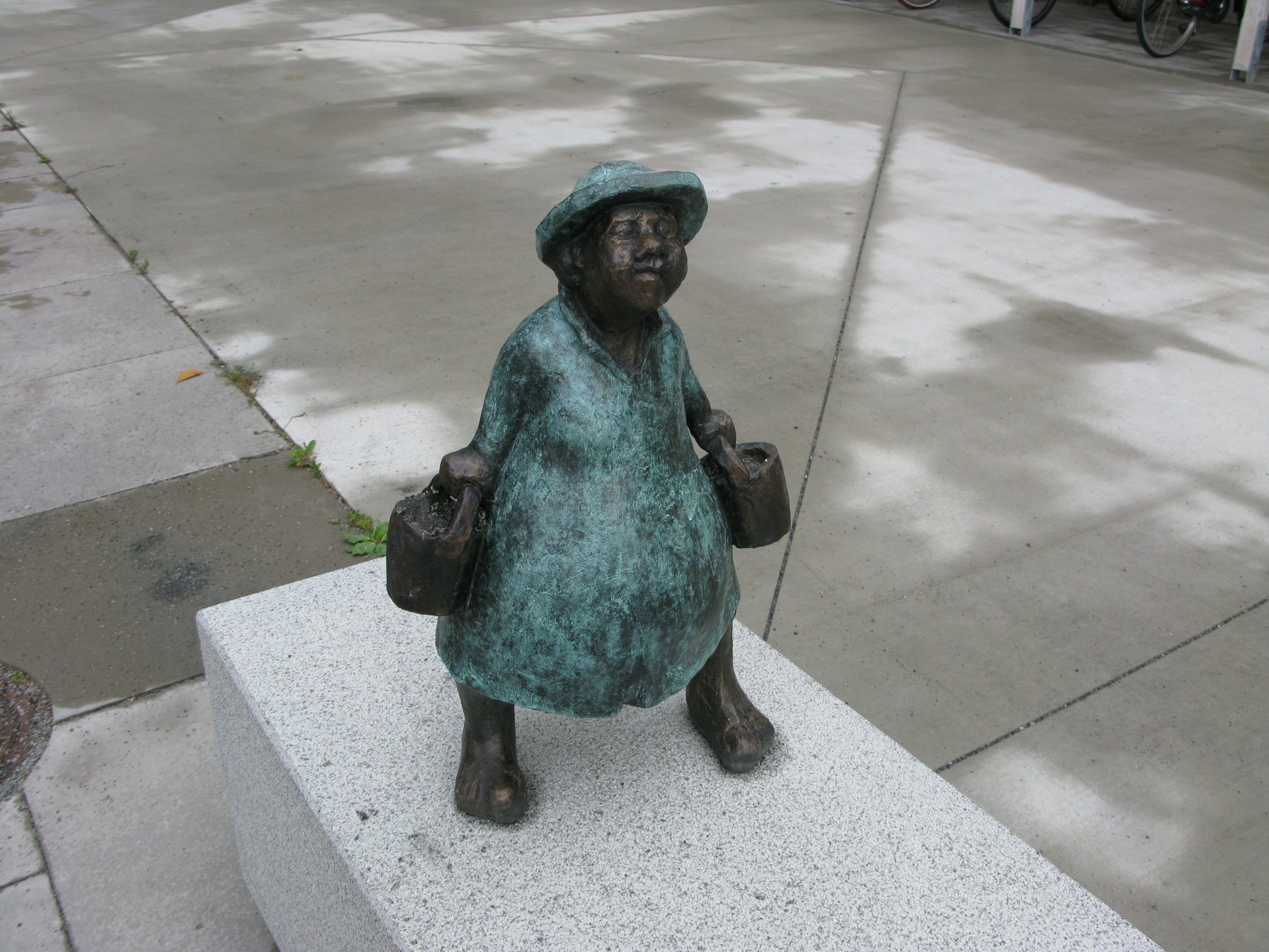 Dam med hatt som bär vatten i två hinkar.