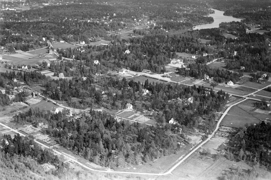 Område med enstaka hus, skogspartier och vägar sett från luften.