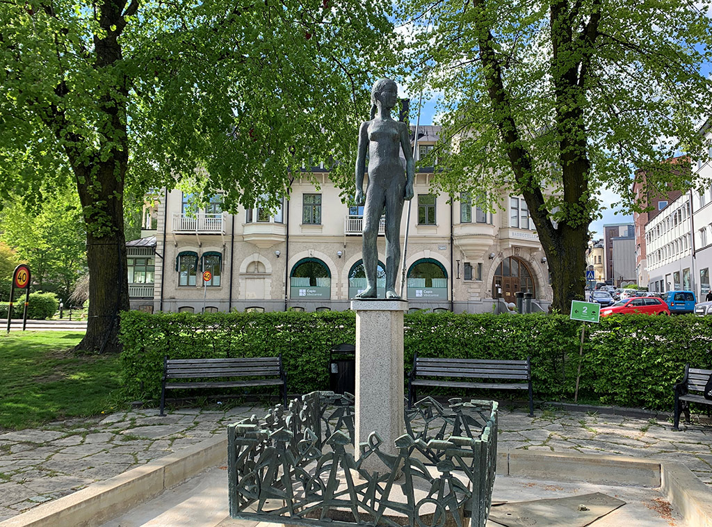 Högt upp på en sockel står en skulptur av en naken flicka.