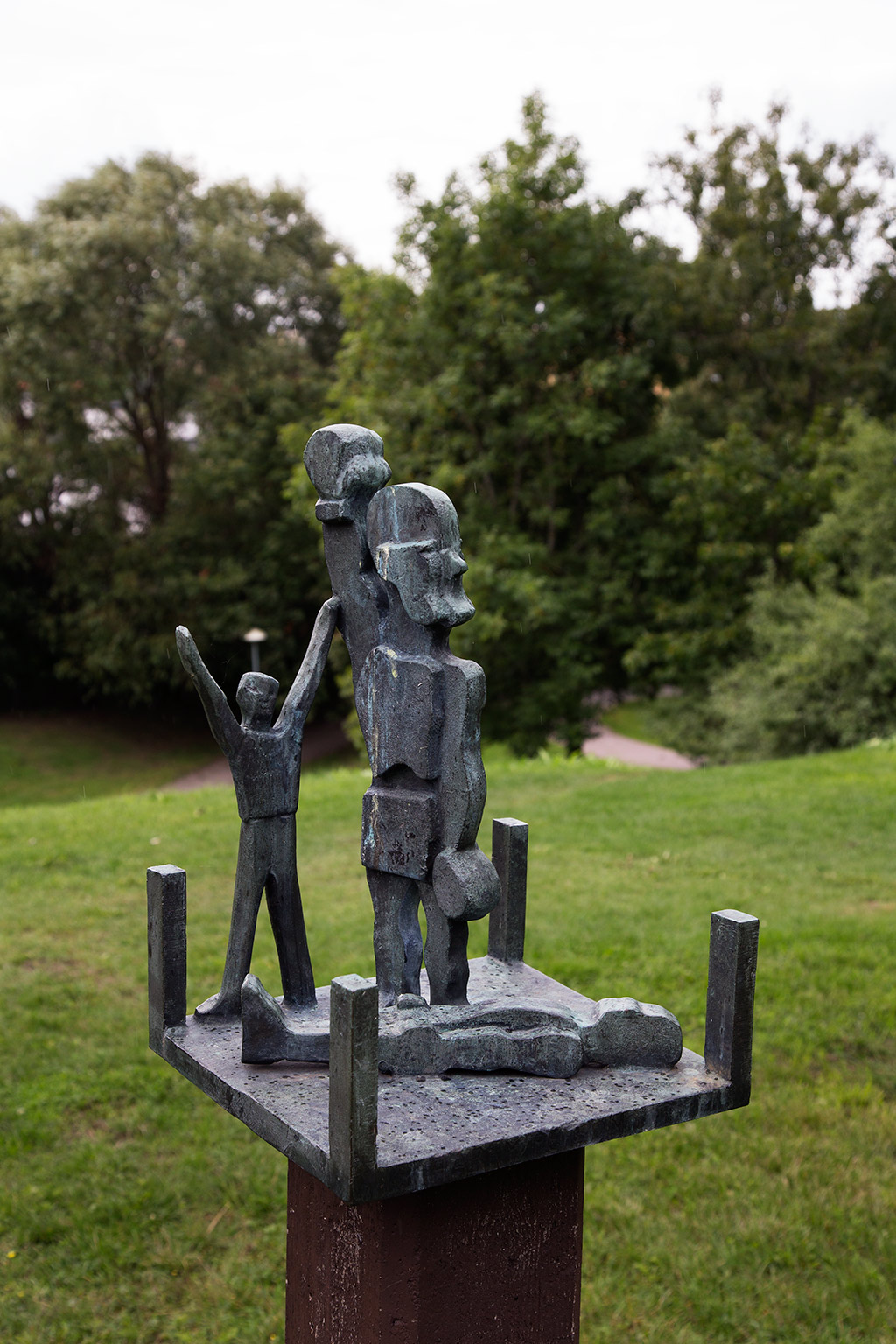 En man står med sträck upp i luften, bredvid ligger en man. Allt är i sten.