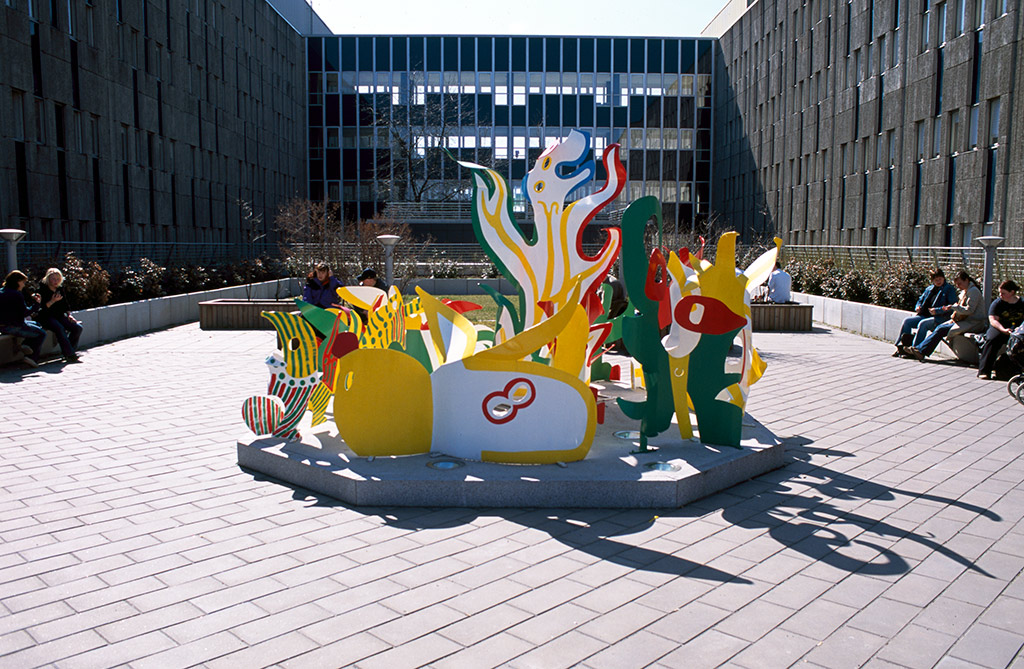 Fantasifulla figurer grönt, gult, rött och vitt står i en ring på en låg sockel.