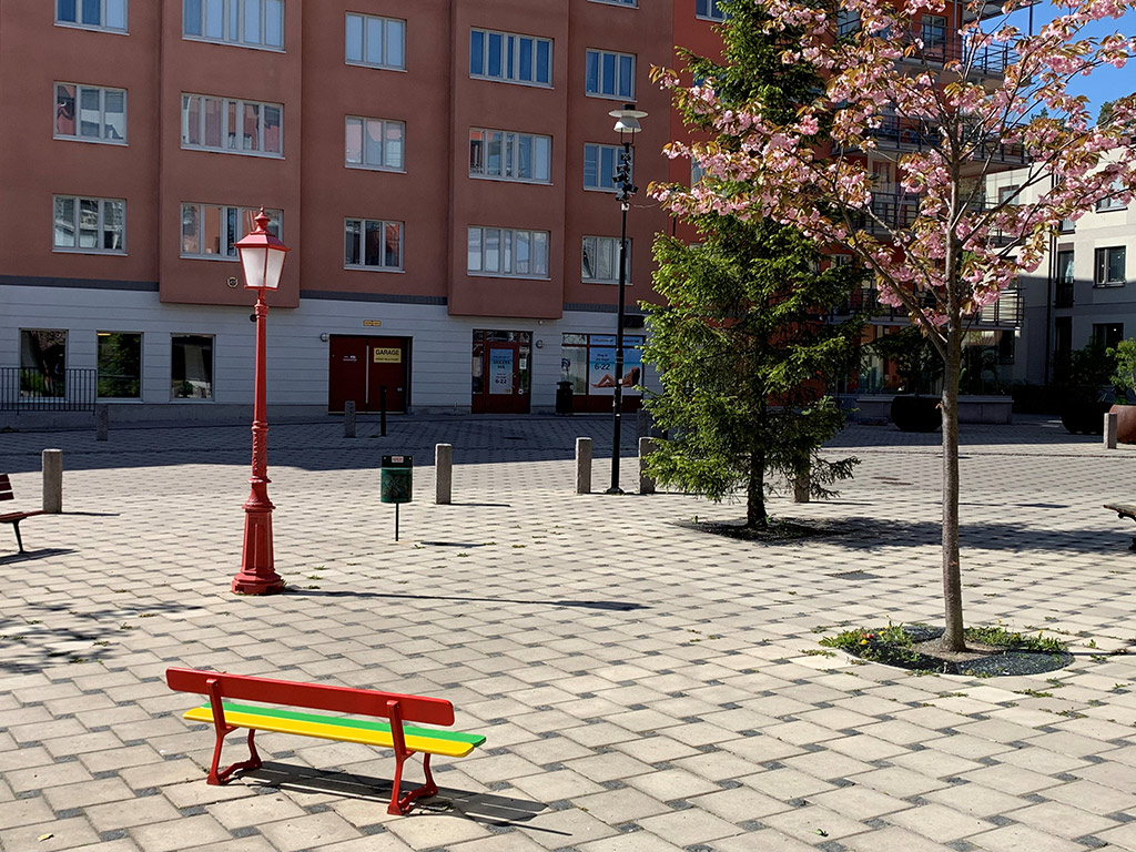Torg med bänkar, blommande körsbärsträd och en gran. Till stora delar taktilt verk.