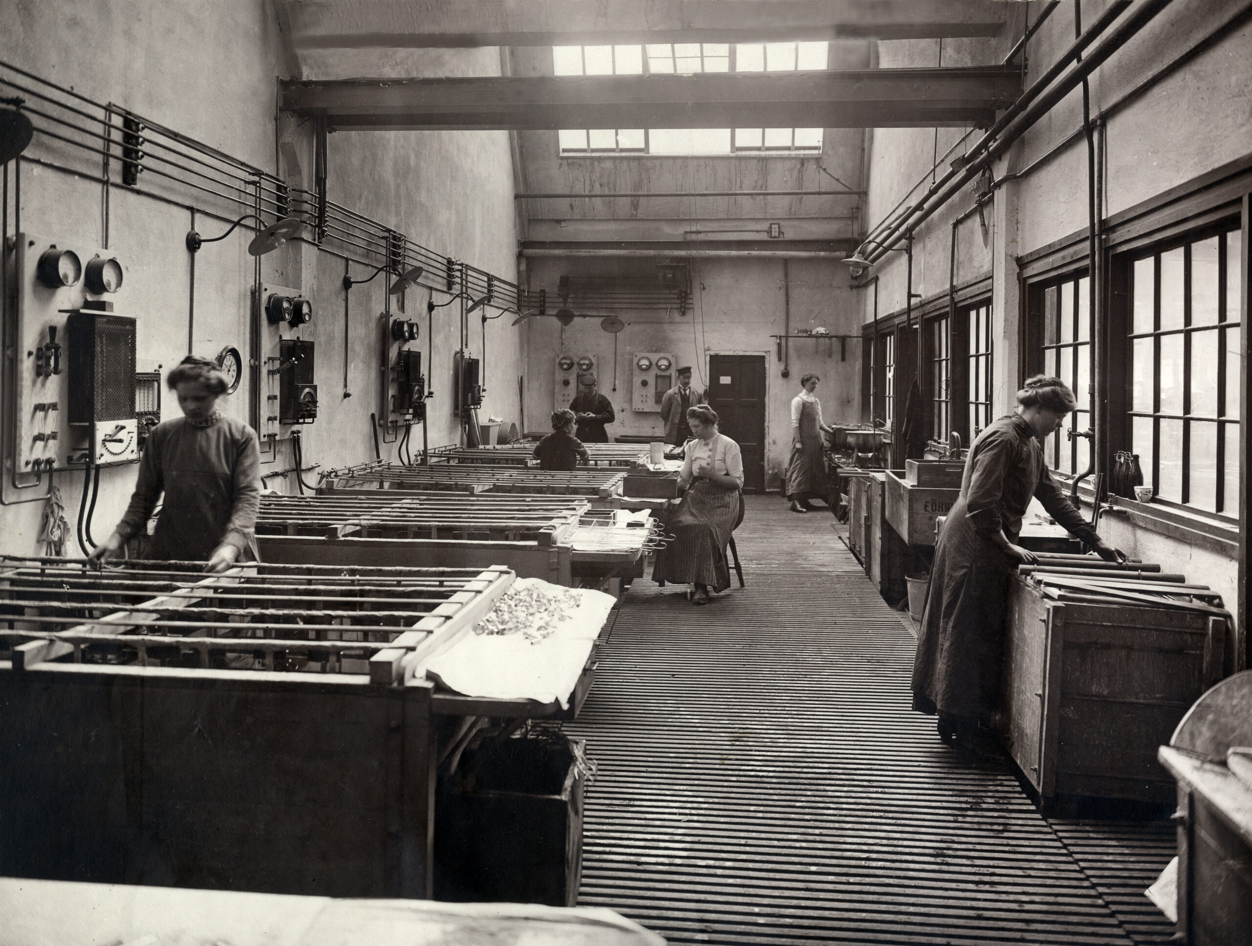 Svartvitt fotografi, några kvinnor och ett par män arbetar i en verkstad.