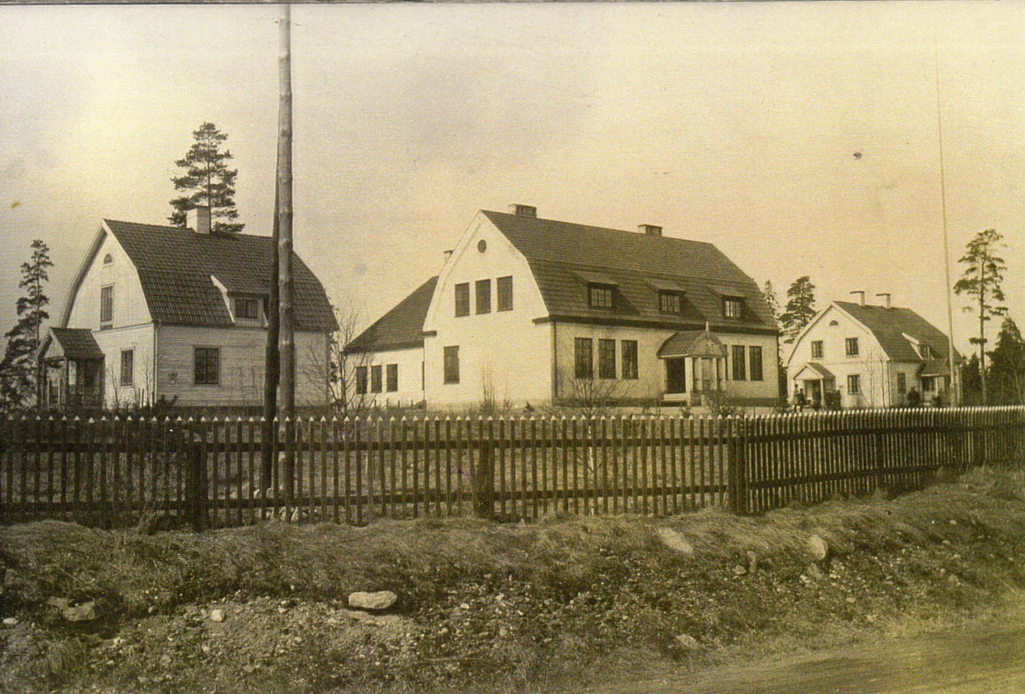 Svartvit bild med fyra vita byggnader. En stor i mitten omgiven av mindre hus.