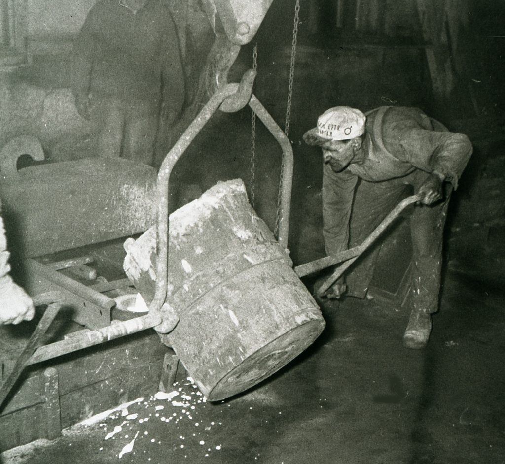 En man med keps böjer sig ner för att välta ut innehållet i en stor behållare.