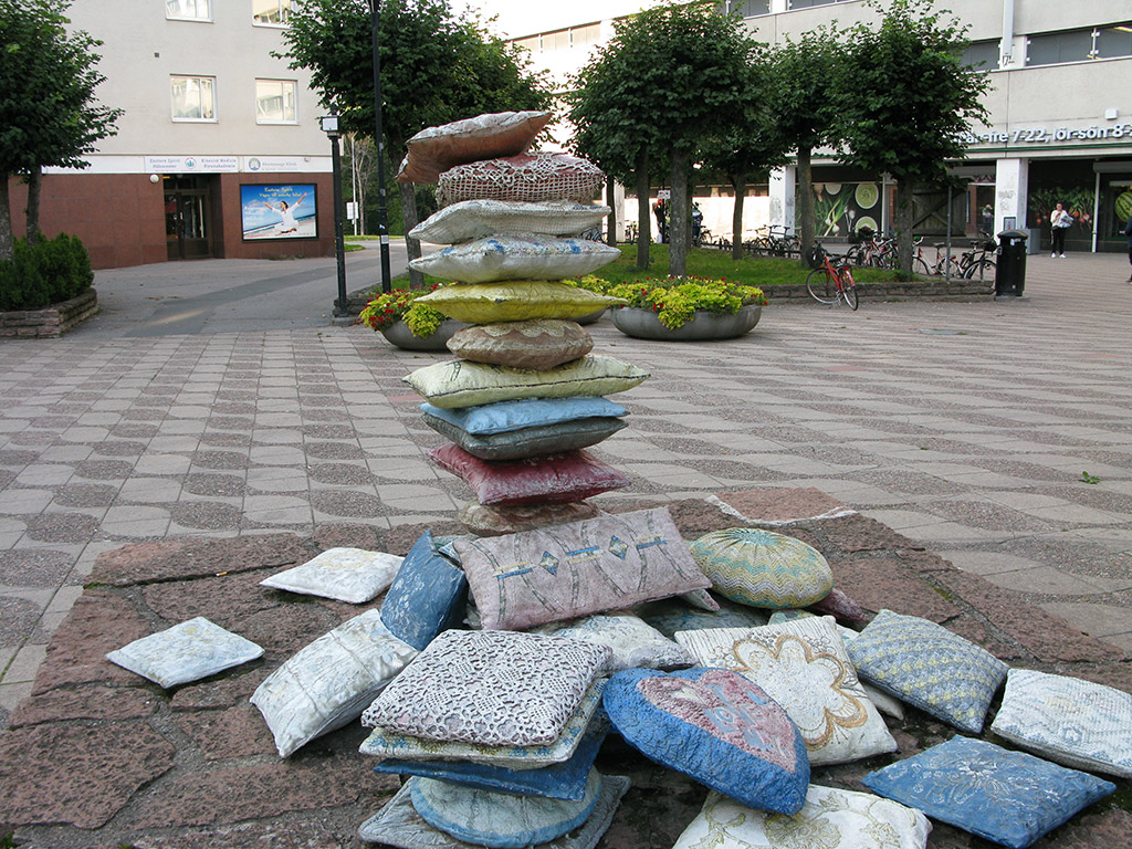 Broderade kuddar i olika färger i en stapel och flera kuddar runtomkring