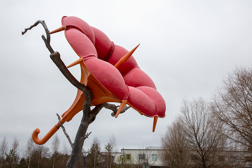 Skulptur av en röd blomma med paraplyskaft i ett träd.