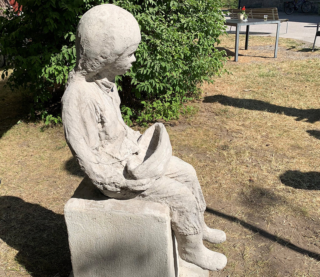 Skulptur av flicka som sitter med en båt i händerna.