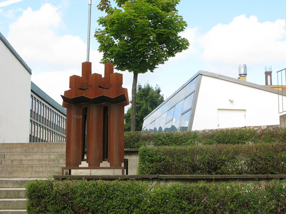Skulptur med fem figurer i rostig färg som står i en trappa utomhus.