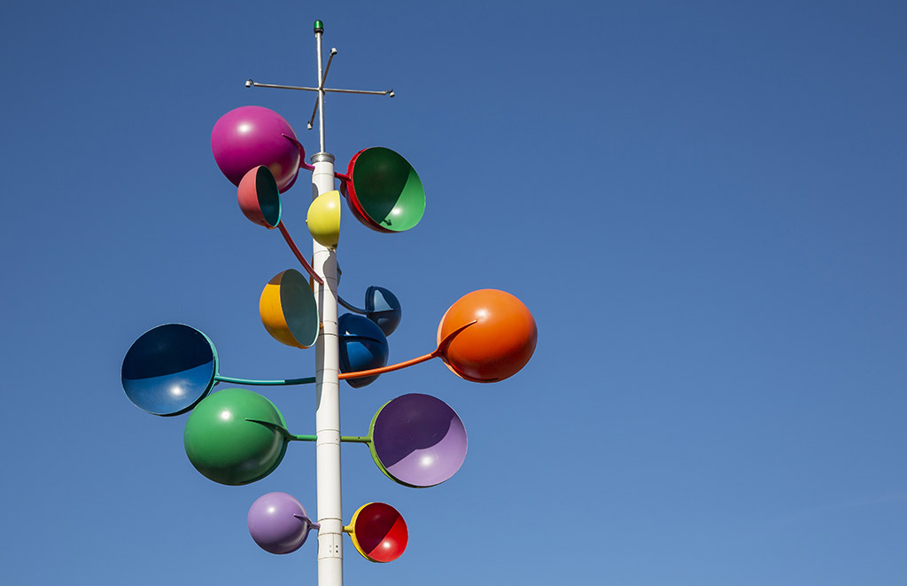Runda former i olika färger som blå, orange, rosa och grön på en vit stång mot en blå himmel.