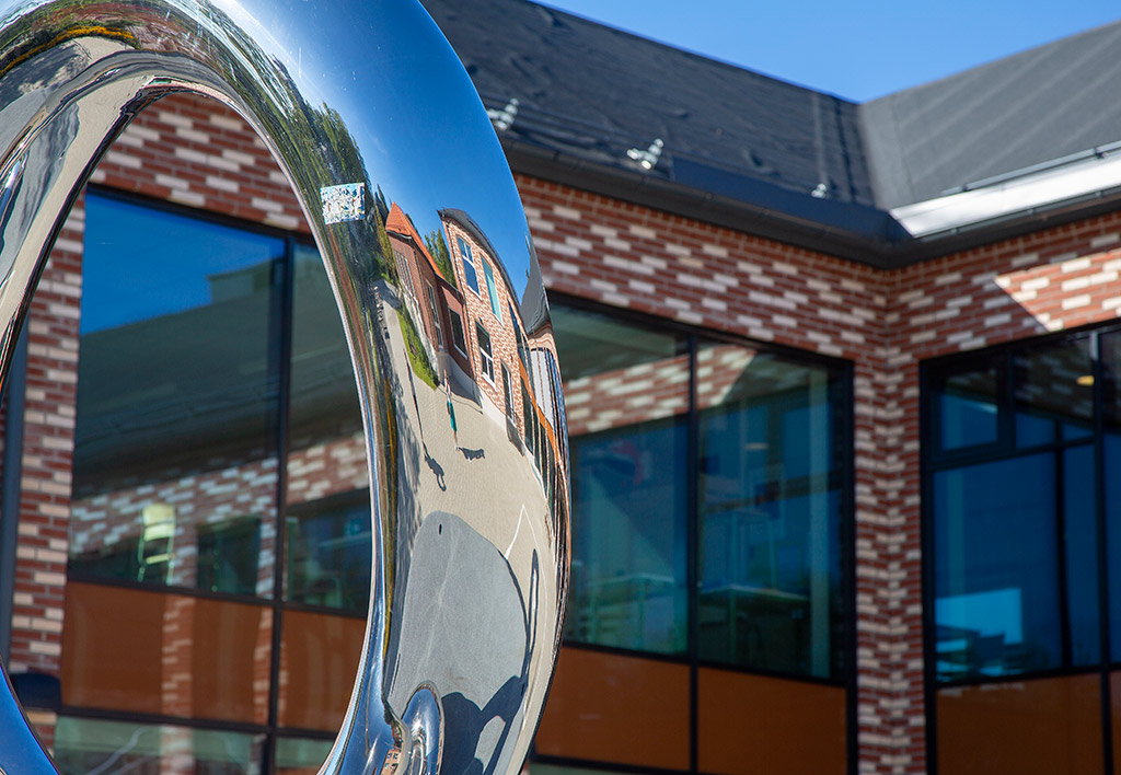 Silverglänsande rund form framför en brunröd byggnad.