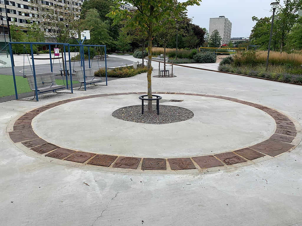 Många bilder i brunt på grå betong på marken som bildar en ring runt ett träd.