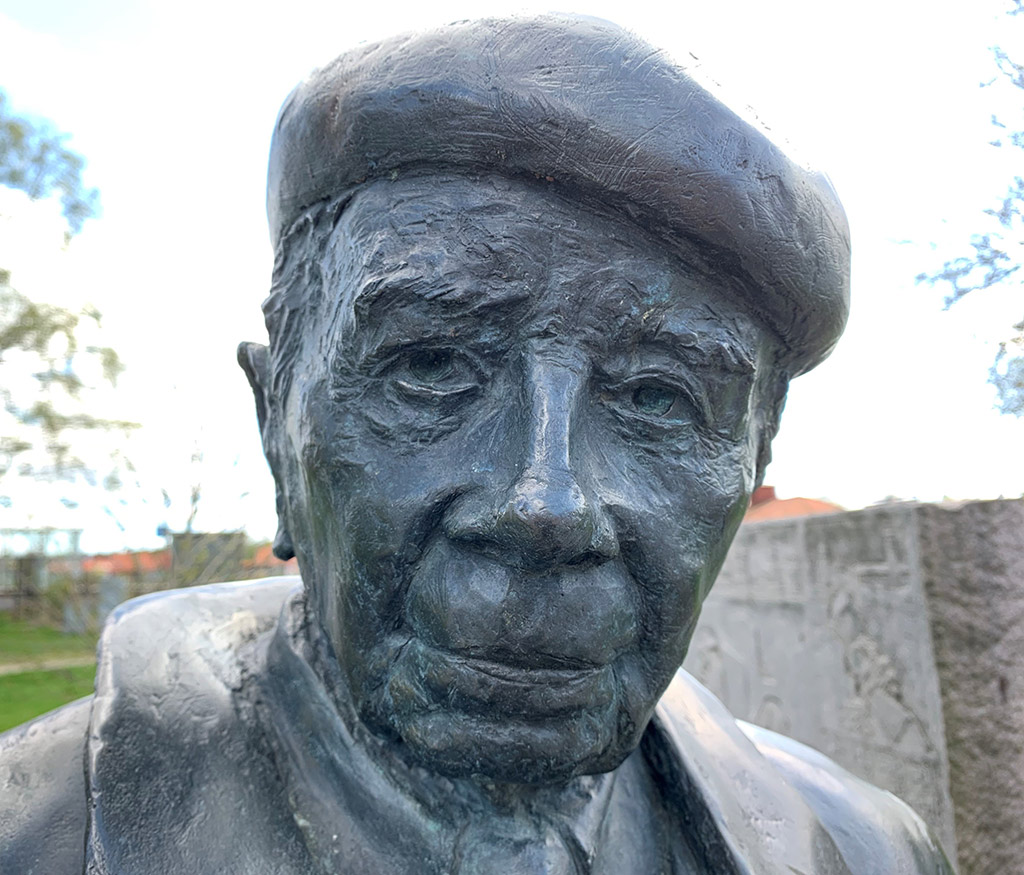 Bronsskulptur av en man med basker i utomhusmiljö.