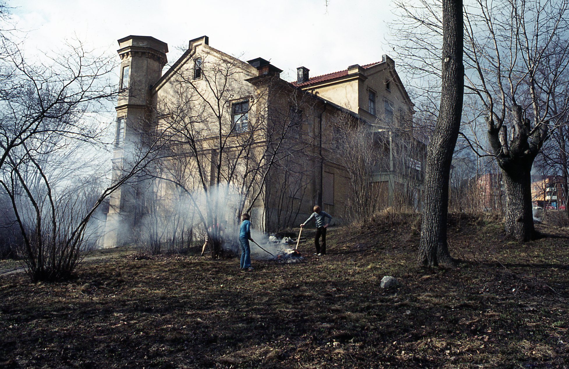 Det ryker från en hög. Två personer petar i elden med varsin pinne. Slottet i bakgrunden.