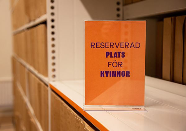 Arkivhyllor fyllda med arkivlådor. På en tom hylla står en skylt med texten "Reserverad plats för kvinnor".