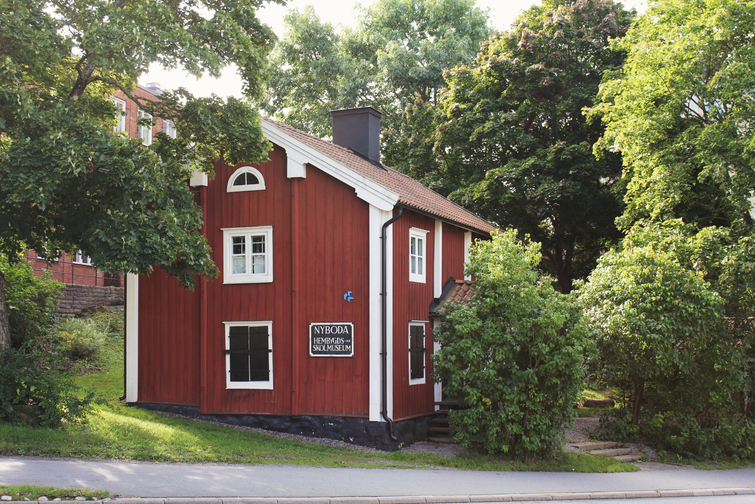 Röd träbyggnad med vita knutar omgiven av träd.