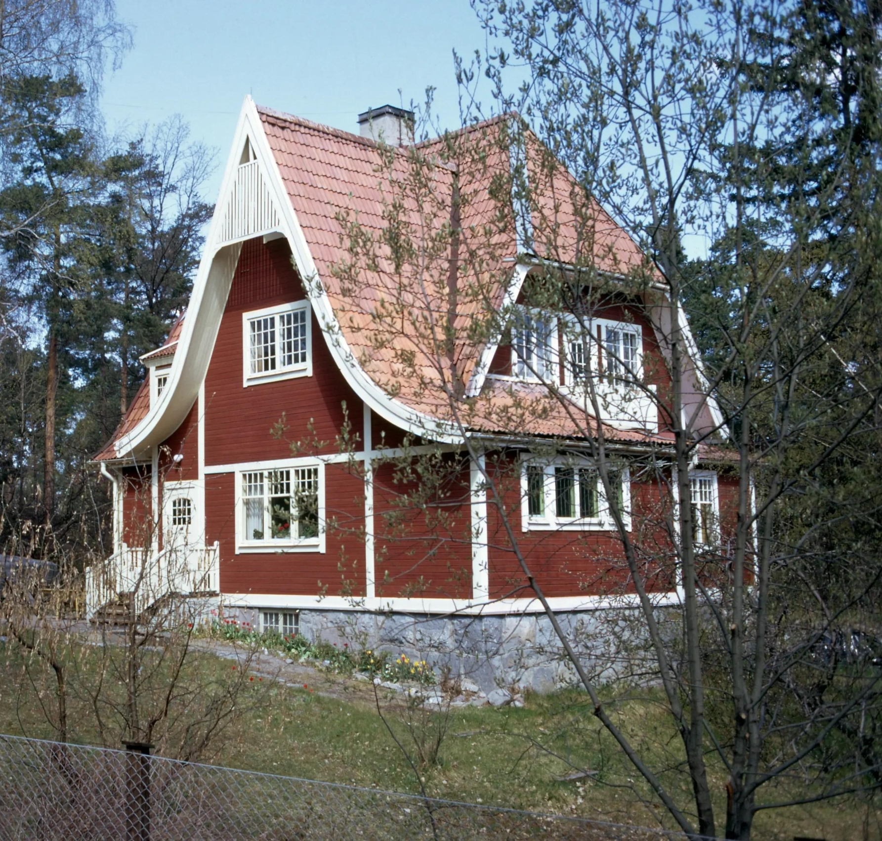 Röd trävilla från sekelskiftet med vita knutar och sluttande tak.