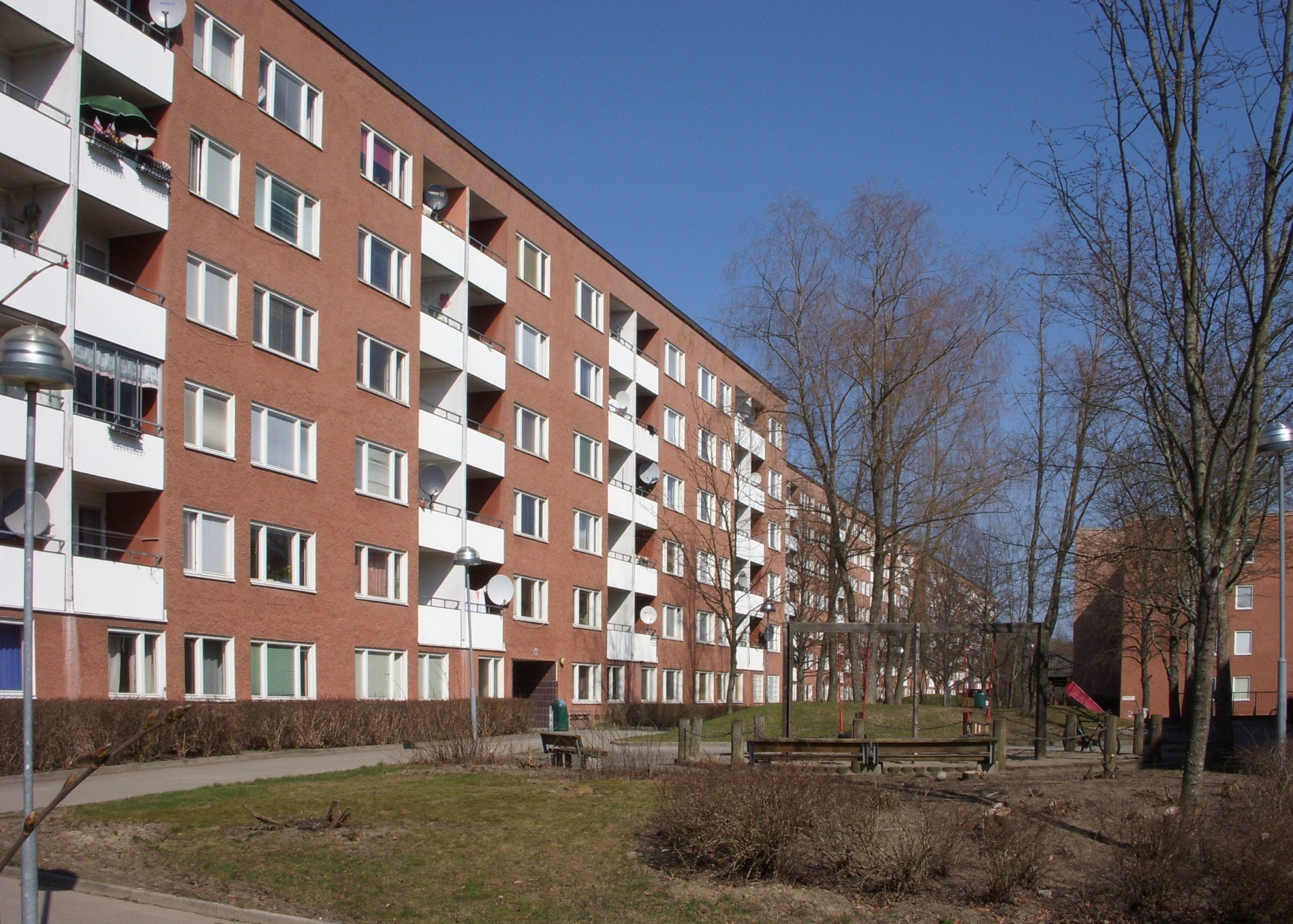 Stor tegelbyggnad med vita plåt balkonger. Lekpark och träd framför huset.
