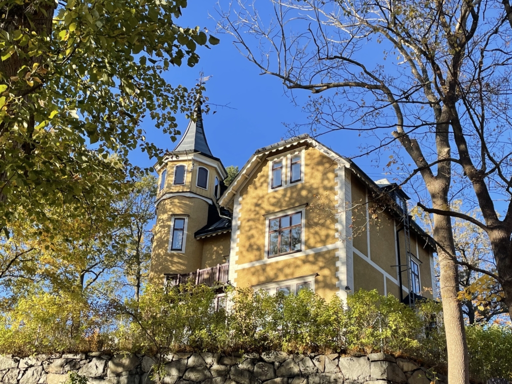 Gul trävilla på höjd med vita knutar och ett torn.