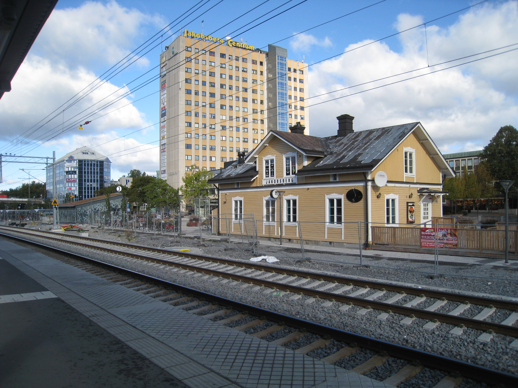 Järnvägsspår med gul träbyggnad bredvid och höghus i bakgrunden.
