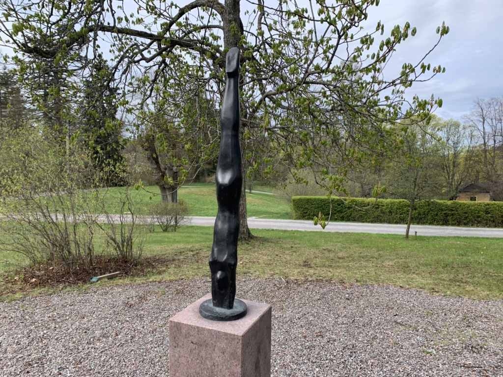 Skulptur föreställande smal person i svart sten, som dyker ner i en piedestal av rosa granit.