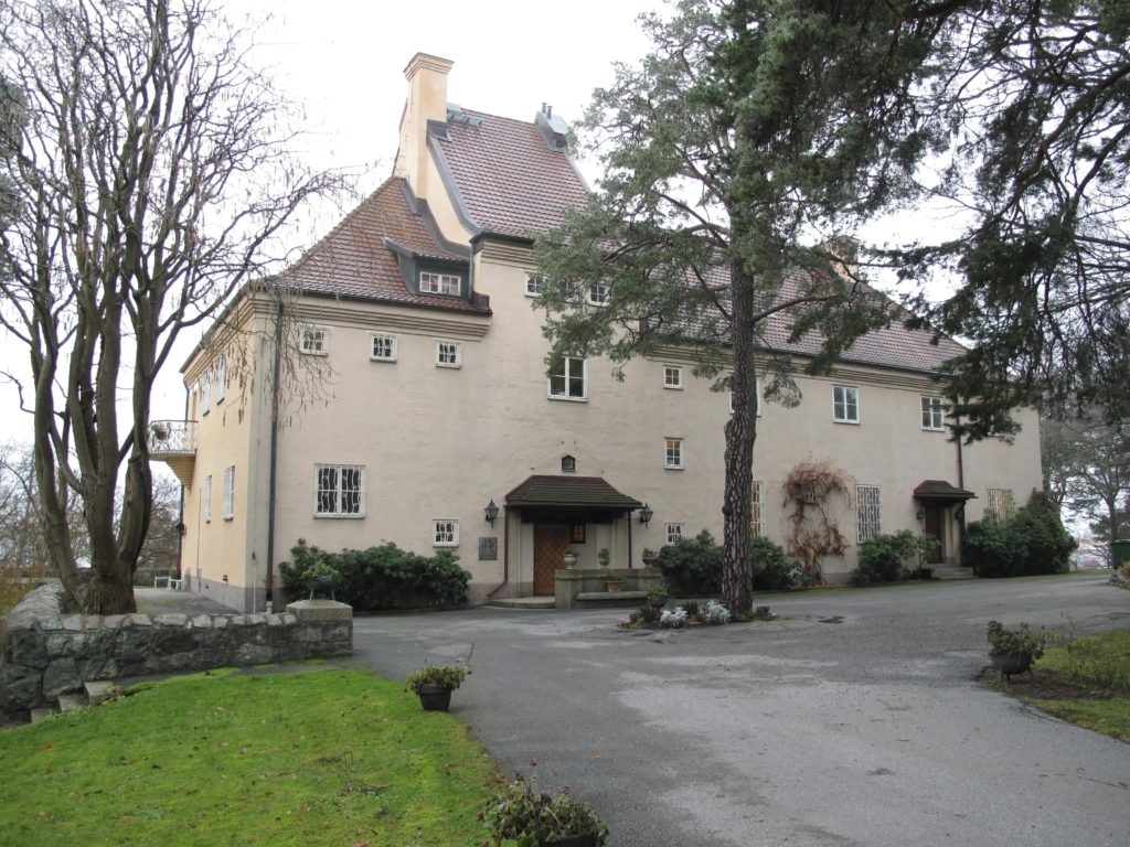 Stor villa från 1910-talet med beige putsad fasad. Bilden är tagen från gårdsplan.