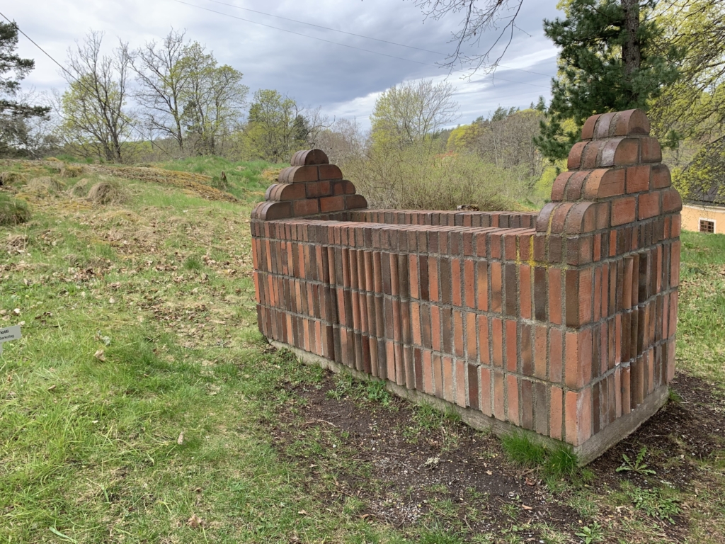 Skulptur i tegel föreställande en rektangulär box med triangulära toppar på kortsidorna.