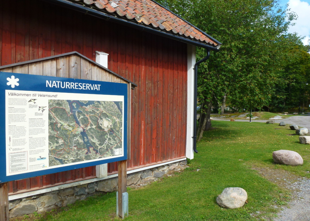 Bilden föreställer knuten av ett rött hus med en skylt framför där det står "naturreservat".