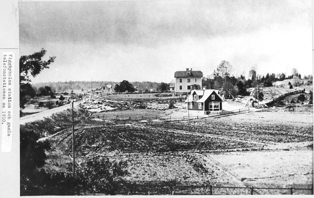 Ett svartvitt foto med ett fåtal hus, åkrar och stängsel.