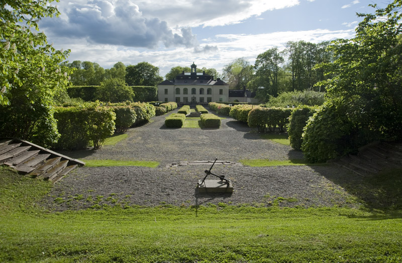 Slottspark med herrgårdsbyggnad i bakgrunden. Staty med ankare syns i förgrunden.