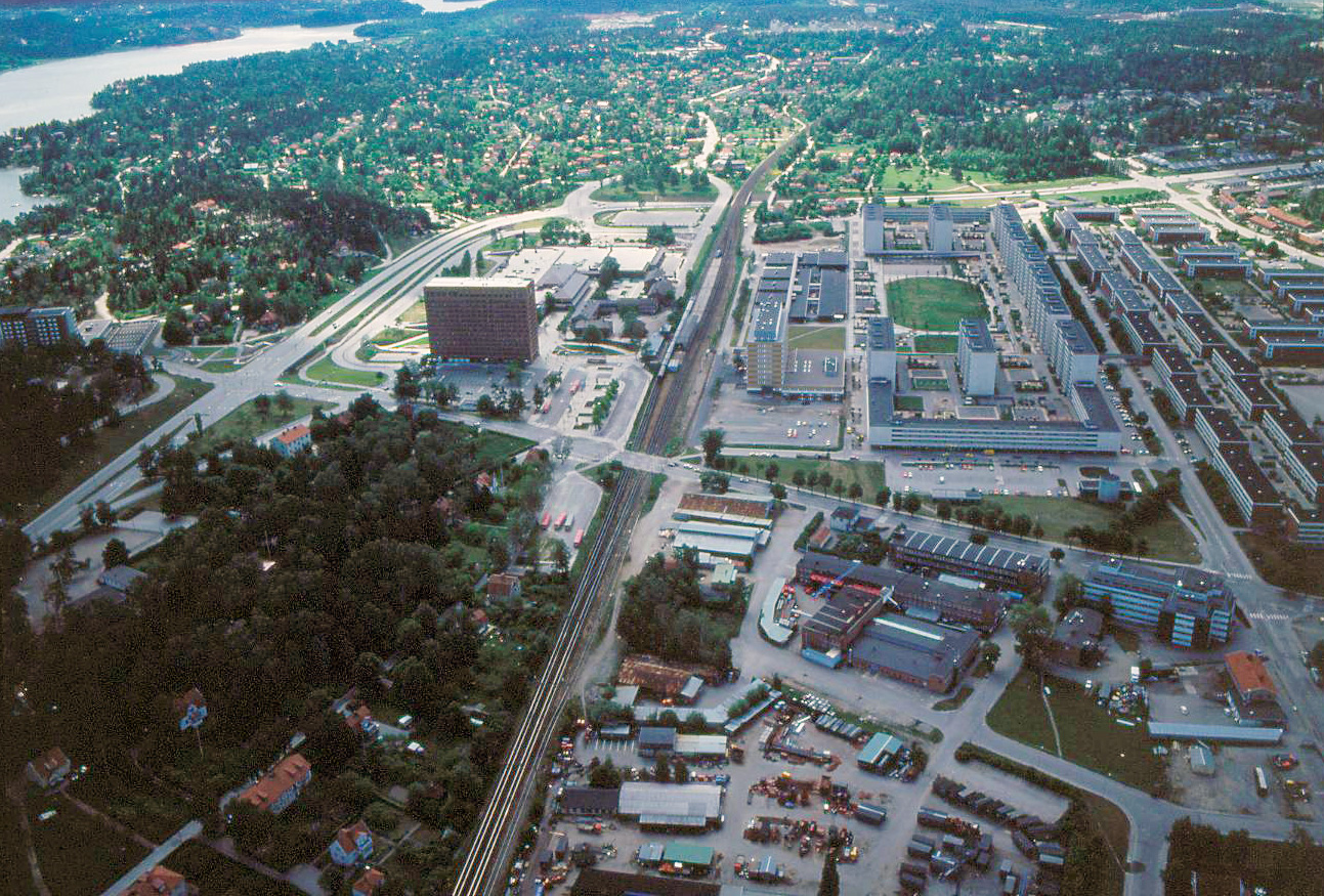 Centrum i förgrunden, längre bort villor omgivna av grönska och en vik. Järnvägen går rakt igenom bilden.