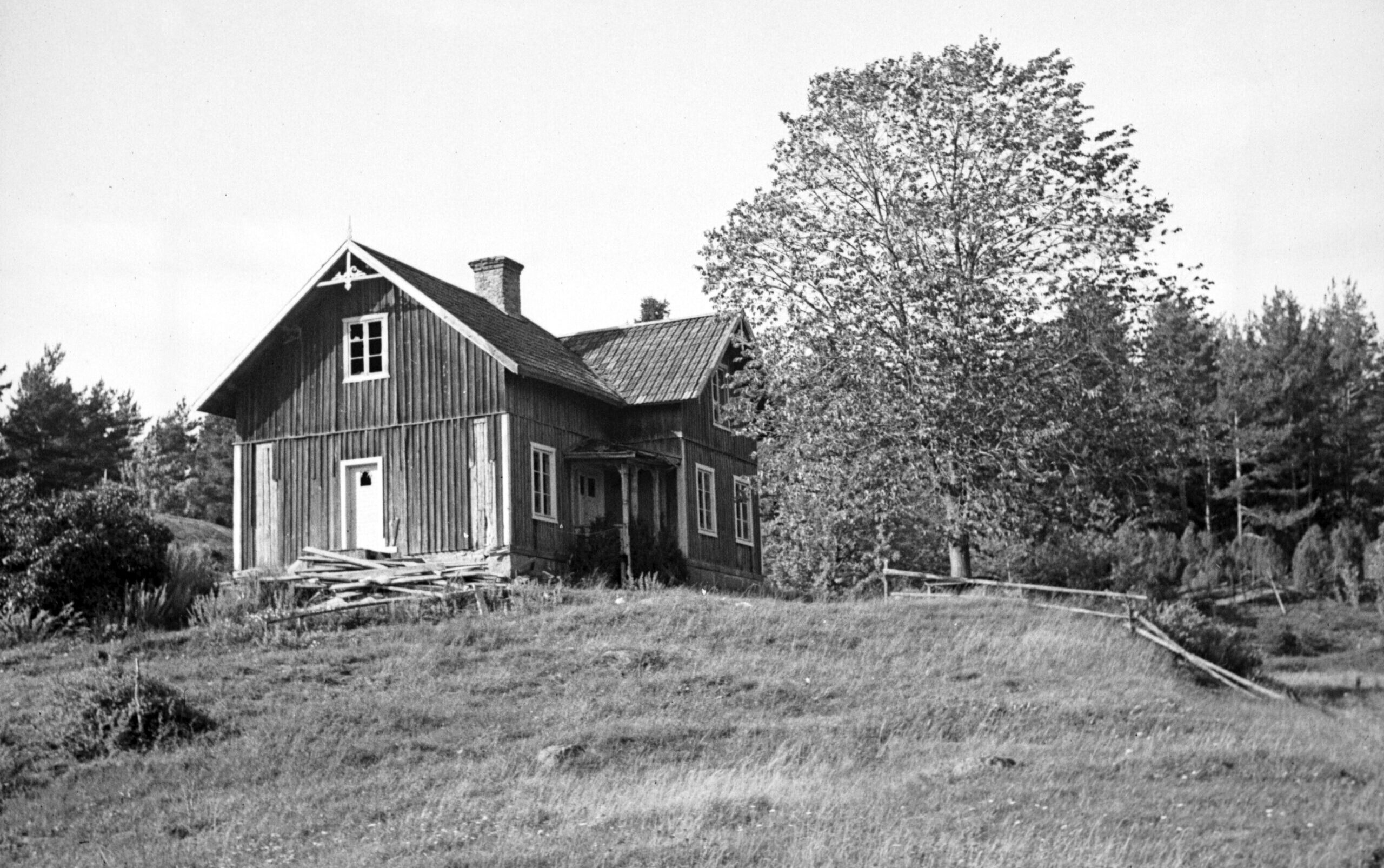 Ett hus i vinkel på en kulle. Några panelbrädor har lossnat och ligger i en hög framför huset. Sommar.