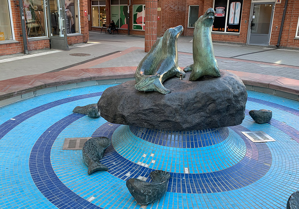 Skulptur med tre sälar på en sten i blå fontän.