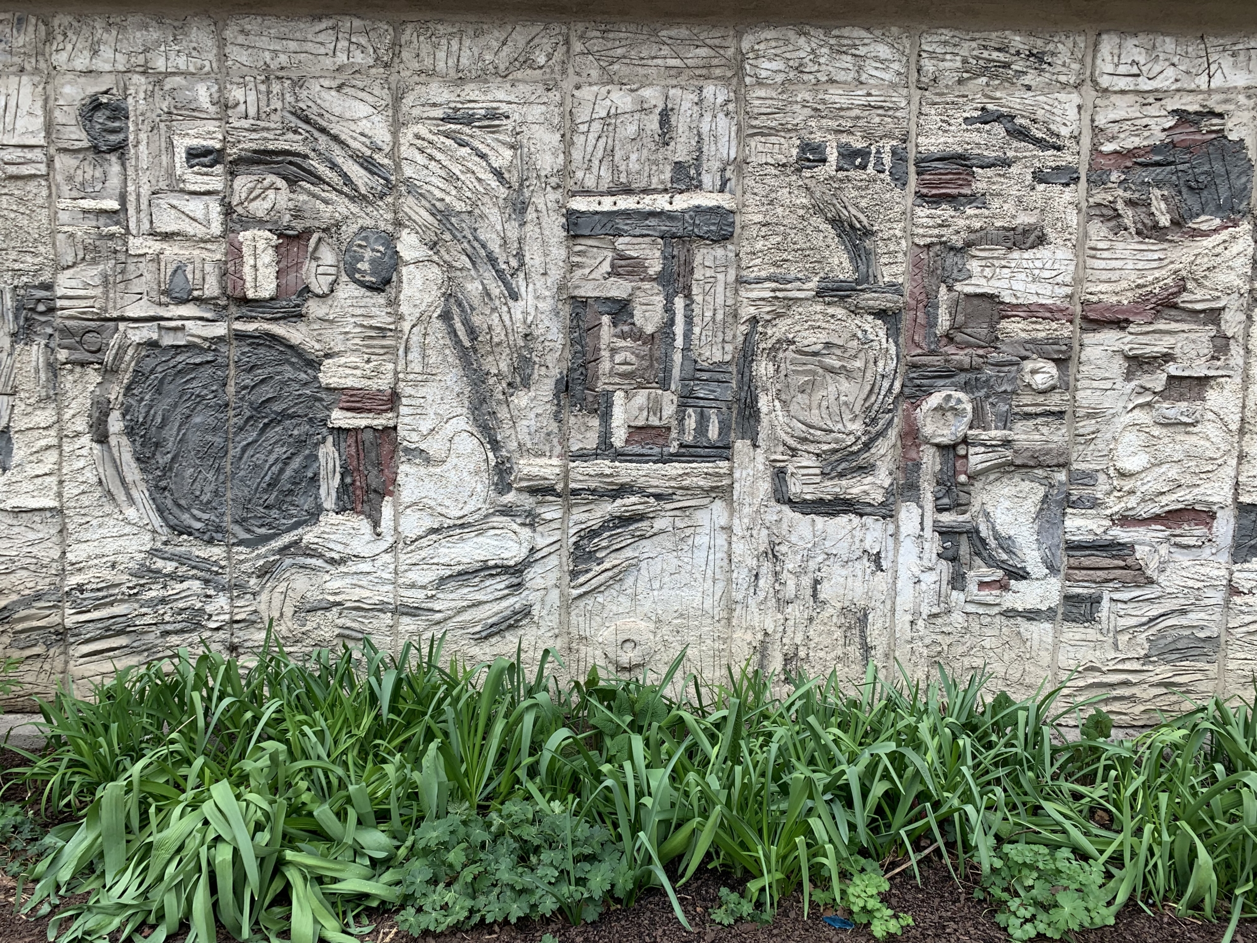 Abstrakt konstverk på en husfasad. Betong i grått, beige och vitt med reliefverkan och ristningar.