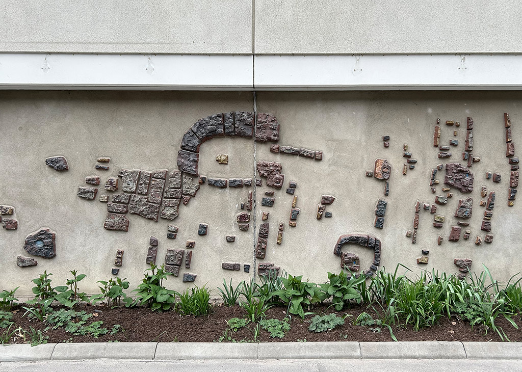 Abstrakt konst på betongvägg. Bitar av betong i olika färger som tegelrött, guld och blått bildar ett oregelbundet mönster.