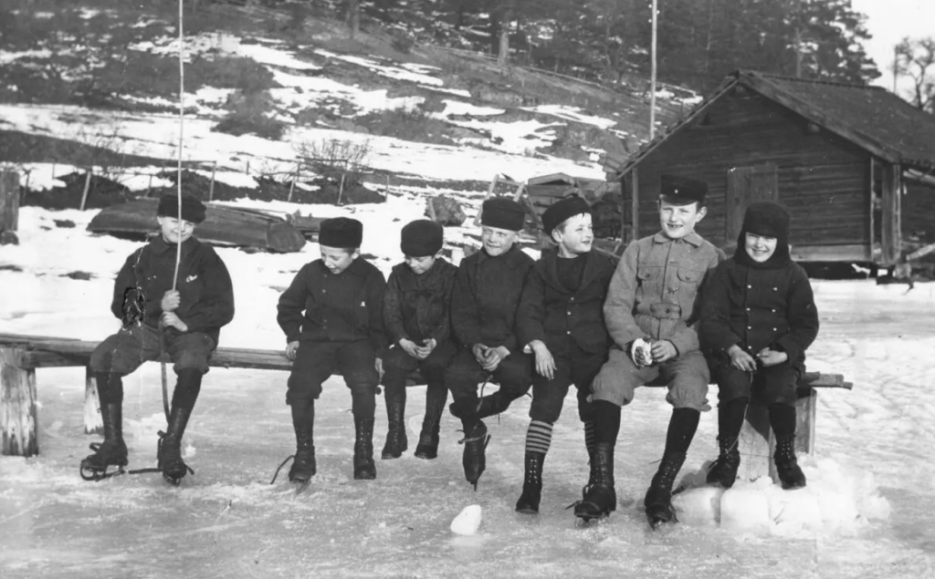 Sju pojkar på en bänk på isen. Några har skidskor.