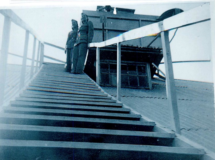 Två kvinnor i uniform på en trappa på ett tak. En tredje skymtas med en kikare.