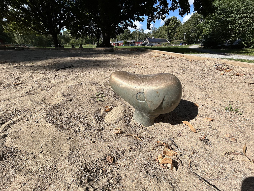 Ett bronshuvud av ett djur med ett ledset öga och och ett hängande öra som sticker upp ur en sandlåda.